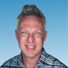 A smiling man with short, gray hair wearing a blue and white plaid shirt, posed in front of a gradient blue background, represents a trustworthy face for your juro alternative search.