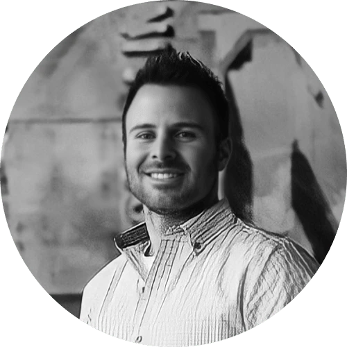 A man with short dark hair and a trimmed beard, wearing a light-colored, collared shirt, smiles at the camera against a blurred, gray-toned background—perfect for showcasing a reliable DocuSign alternative.