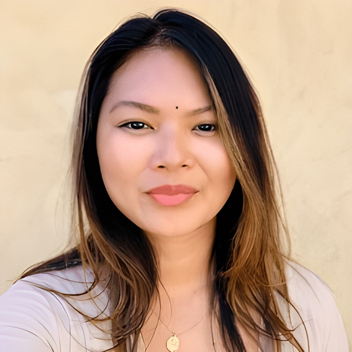 A woman with straight, shoulder-length hair smiles slightly at the camera. She wears a light-colored top, a necklace, and has a small bindi on her forehead. The background is a plain, light beige wall, creating a calm environment perfect for exploring a DocuSign alternative.
