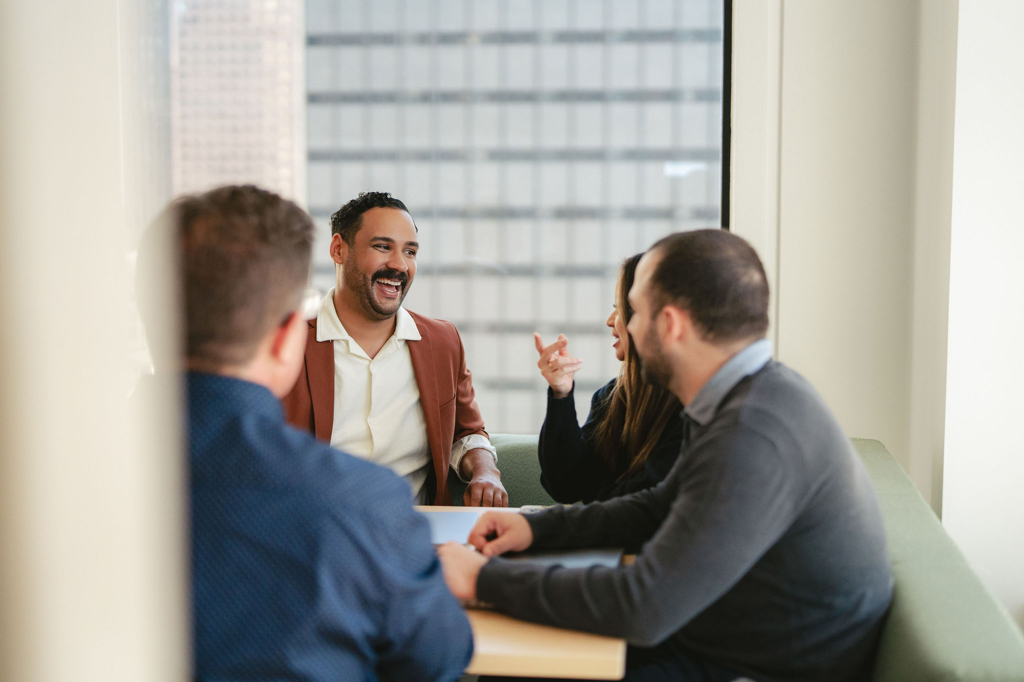 Four people sit around a table in a modern office, engaged in buy-side conversation.