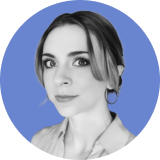 Black-and-white headshot of a woman with light hair, styled with a center part and loose waves, wearing hoop earrings and a collared shirt. An ironclad CLM blue circle forms the solid background.