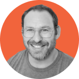 Smiling man with glasses and a beard, wearing a t-shirt. The photo is black and white, centered in a circular orange background, symbolizing the approachable expertise behind Ironclad CLM.