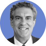 Smiling man with short, wavy gray hair, wearing a suit and tie, featured in a black and white portrait against a circular blue background—an ideal image for an ironclad CLM professional profile.