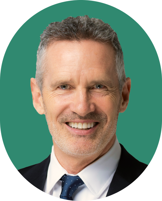 A middle-aged man with short gray hair and a trimmed beard, wearing a suit, white shirt, and polka-dot tie, smiling in front of a solid green background.