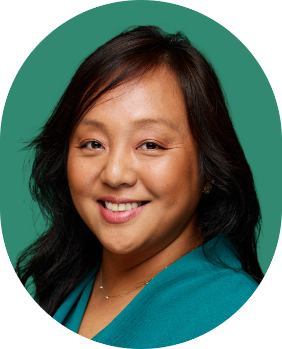 Portrait of a woman with long dark hair and a teal blouse, smiling in front of a solid green background.