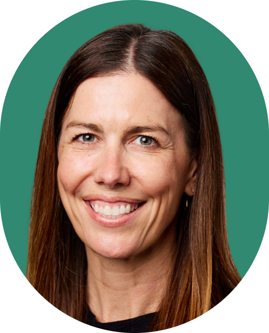 A woman with straight brown hair and a bright smile, wearing a black top, poses in front of a solid teal background.